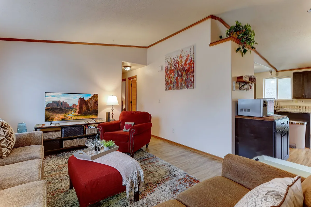 A cozy living room scene featuring a striking red armchair, a television display, a decorative painting, and a central coffee table. The room is filled with inviting touches, suggesting a space ideal for relaxing, socializing, or unwinding after a busy day.