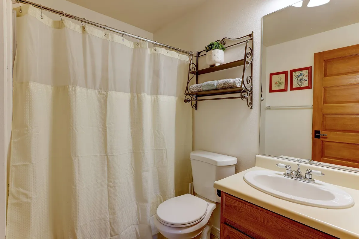 A modern, organized bathroom featuring a walk-in shower hidden behind a shower curtain, a well-stocked shelf with towels, a bathroom mirror, and a wooden door. The overall look is fresh, tidy, and tranquil.