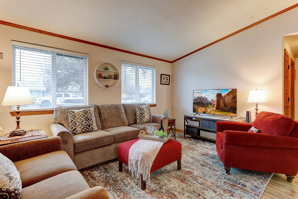 A warm and inviting living room featuring a plush sofa, a vibrant red armchair, a stylish coffee table, and a cozy rug set before a modern television—bathed in natural light and perfectly arranged for relaxation or social gatherings.