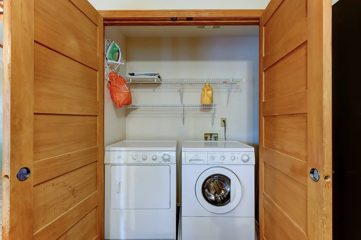 A tidy and functional laundry area featuring a washing machine and dryer, with a shelf above holding assorted cleaning supplies. The space is organized and practical, ideal for handling outdoor gear or laundry after a day of adventure.