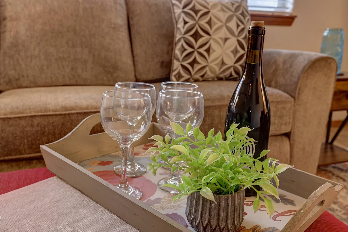 A cozy indoor coffee table is set with a wine bottle, two glasses, a decorative plant, and a tray, inviting guests to unwind with a drink. The setting is intimate, hinting at relaxed evenings in after a day out exploring.