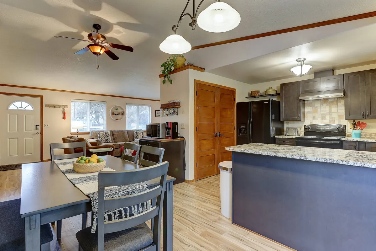An inviting view of the central living area, featuring a comfortable sofa, a dining table with a fruit bowl, and a kitchen counter equipped with appliances. Everything is seamlessly connected, illustrating the flow between dining, living, and kitchen spaces.